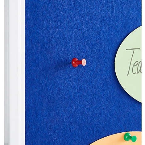 A red pushpin is in a blue felt board, next to a green card with writing.