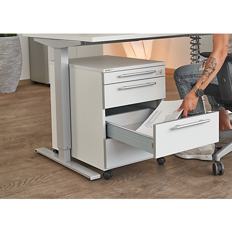 Person opening a drawer of a white mobile pedestal under a desk. Papers are inside.