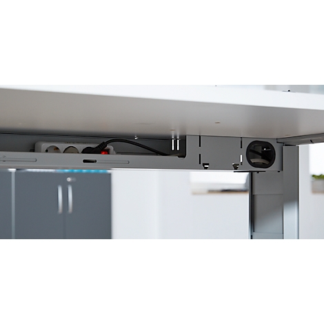 Underside of a table with power strip, cables and cable grommet. The red switch on the power strip is illuminated.