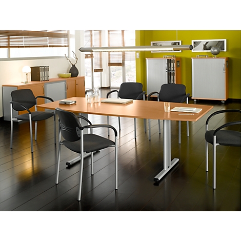 A conference room featuring a light wood table, black chairs, and windows. A long light bar hangs above the table.