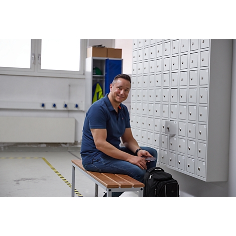Man sitting on bench in front of lockers, smiling at camera.