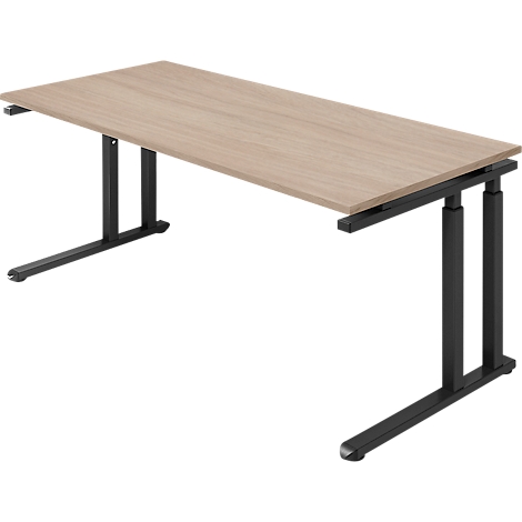 Ein helles Holz-Schreibtisch mit schwarzem Metallgestell. Die Tischbeine sind höhenverstellbar. Perspektivische Ansicht.