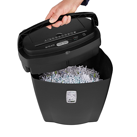 A person lifts the lid of a black paper shredder. The container is filled with shredded paper.