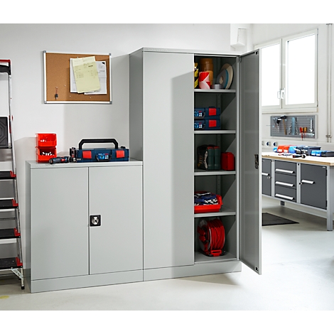 Grijze werkplaatskast, deur open. Gereedschapskist, prikbord, plank met gereedschap. Lichte werkplaats.