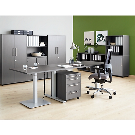 Office with grey furniture and a height-adjustable desk. A laptop, a lamp, office supplies and folders are on the table.