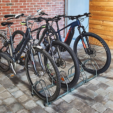 Plusieurs vélos sont stationnés dans un porte-vélos en métal devant un mur de briques.