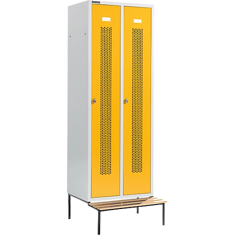 Un armario pintado de amarillo y blanco con dos puertas. Ambas puertas tienen un patrón de agujeros y una abertura de ventilación. Delante del armario hay un banco.