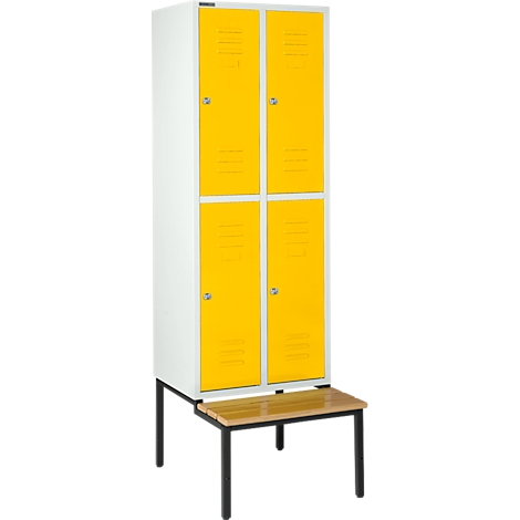 Taquilla blanca con puertas amarillas y banco. De pie sobre patas oscuras, con manijas y ranuras de ventilación.