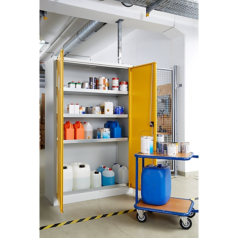 Ein Lagerraum mit einem gelb getäfelten Schrank, der mit Behältern gefüllt ist, daneben ein Rollwagen mit einem blauen Kanister.