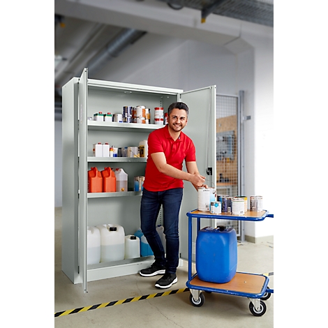 Ein Mann in rotem Polohemd steht vor einem grauen Schrank. Er nimmt Farbeimer vom Rollwagen.