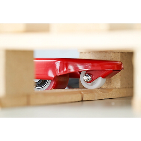 Gros plan d'un chariot de transport rouge avec des roues blanches, partiellement visible dans un cadre en bois.