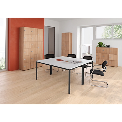 Ein Büro mit Holzböden, weissem Tisch, schwarzen Stühlen und Schränken. Ein Fenster lässt Tageslicht herein.