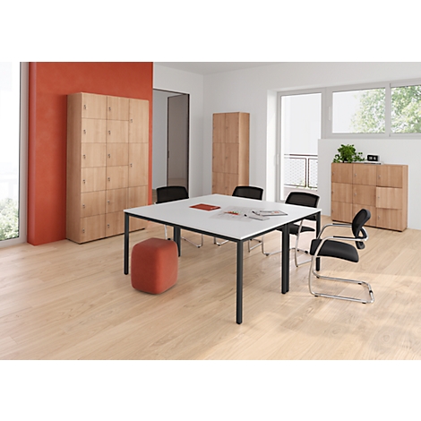 Ein heller, moderner Büroraum mit einem Tisch, Stühlen und Schränken. Roter Akzent an Wand und Hocker.
