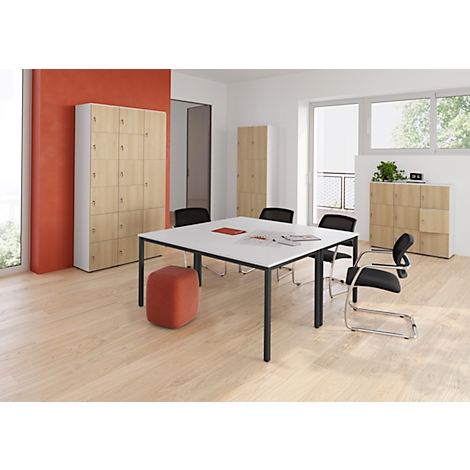 Ein heller Konferenzraum mit Tisch, Stühlen und Schränken. Ein roter Hocker steht vor dem Tisch.