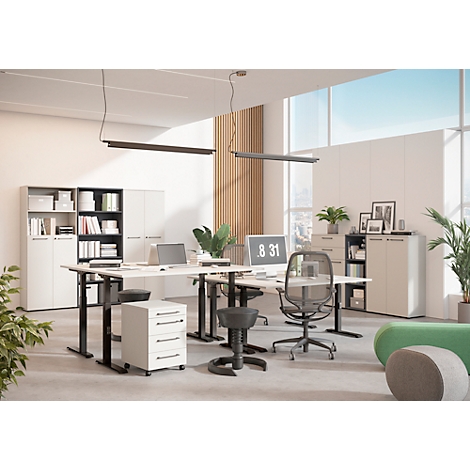 Büro mit höhenverstellbaren Schreibtischen, Bürostühlen und Schränken. Auf dem Monitor steht 8:31. In der Ecke steht eine grüne Couch.