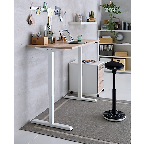 Schreibtisch in hellem Holz mit Laptop, Zubehör und Pflanzen, darunter ein höhenverstellbarer weißer Tisch und ein schwarzer Hocker.