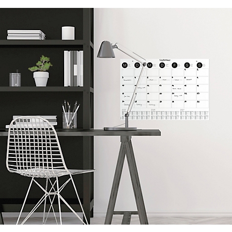 Schreibtisch mit Kalender, Lampe und Stuhl. Auf dem Kalender steht September. Ein Regal steht an der Wand.