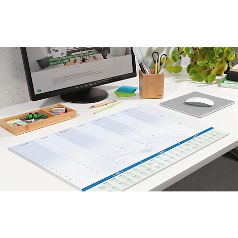 Ein Schreibtisch mit Wochenplaner, Computer und Büroausstattung. Der Planer ist im Fokus.