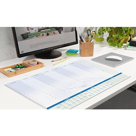 Ein Schreibtisch mit einem grossen Wochenkalender. Auf dem Tisch liegen ein Monitor, Stifte, eine Bambusschale und eine Pflanze.