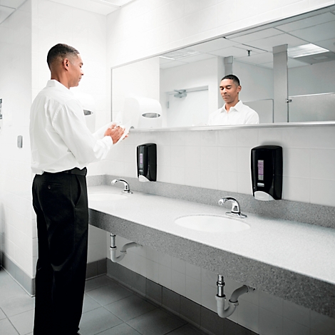 Een man in een wit overhemd droogt zijn handen in een openbaar toilet. Zijn reflectie is te zien.
