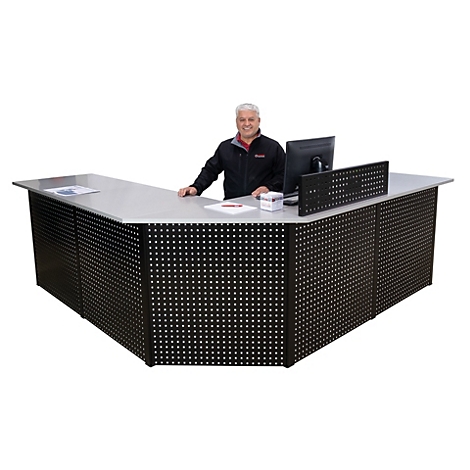 Ein Mann steht hinter einem schwarzen Empfangstresen mit Lochmuster, auf dem ein Computer steht. Er lächelt.