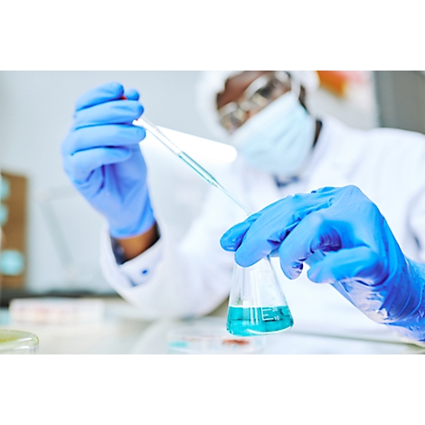 Ein Wissenschaftler mit blauen Handschuhen pipettiert Flüssigkeit in einen Erlenmeyerkolben mit blauer Flüssigkeit.