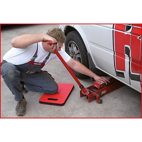 Ein Mann kniet, um einen Wagenheber an einem weißen Transporter zu bedienen. Er benutzt einen roten Hebel, um das Auto anzuheben.