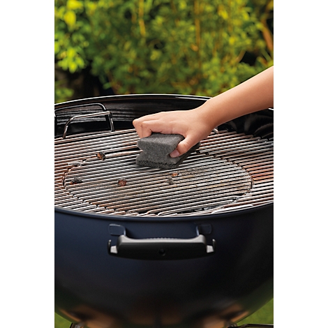 Eine Hand reinigt mit einem Schwamm den Grillrost eines schwarzen Grills.
