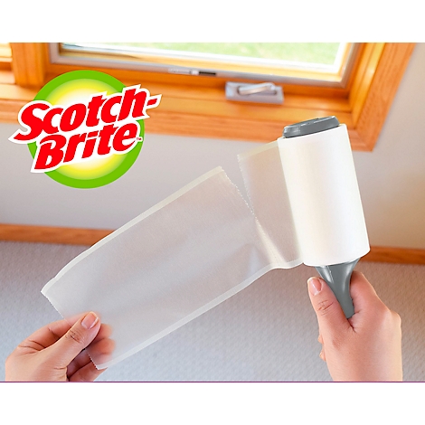 Een persoon houdt een Scotch-Brite-pluisjesroller voor een raam vast.