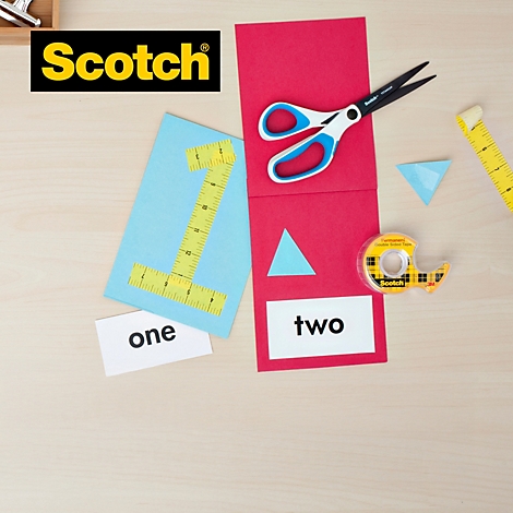 Knutselscène; een blauwe '1' en een rode '2' zijn versierd met schaar, plakband en driehoeken op een houten tafel.