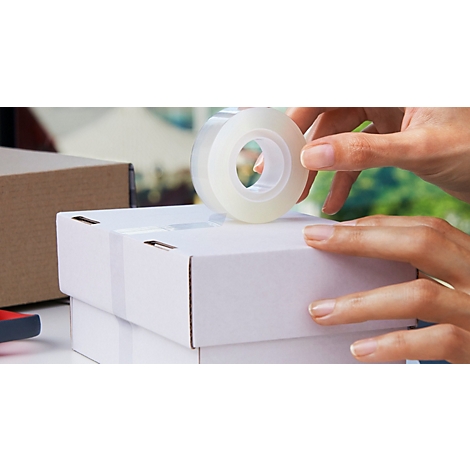 Handen houden een rol transparante Scotch-tape boven een witte kartonnen doos.