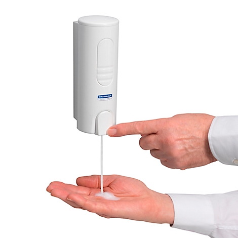 Weiße Seifenspender, ein Finger drückt Knopf. Seife fließt in die Hand, die sich darunter befindet.