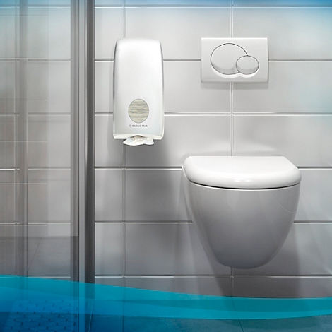 In einem Badezimmer: Eine weiße, wandhängende Toilette mit einem Spender für Papiertücher und einer Spülung.