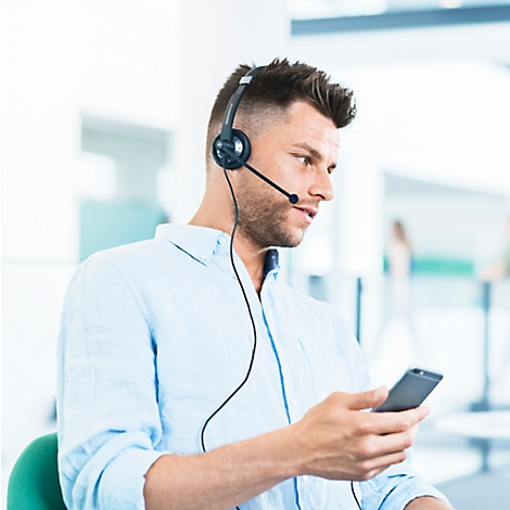 A man with a headset on the phone, looking at his smartphone.