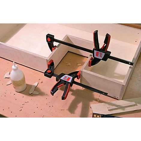 Boîte en bois fixée avec des serre-joints, de la colle et des copeaux de bois sur un plateau de table.