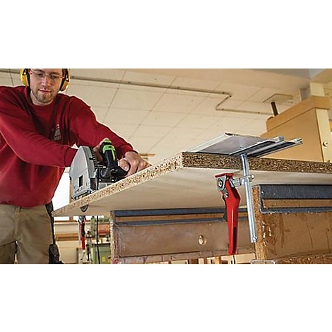 Un homme portant une protection auditive scie un panneau de bois avec une scie circulaire. Un atelier est visible en arrière-plan.
