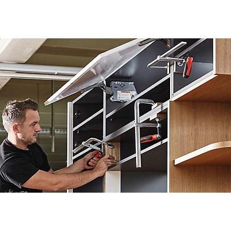 Un artisan assemble des meubles, utilisant une pince et une visseuse sans fil, avec une armoire ouverte en arrière-plan.