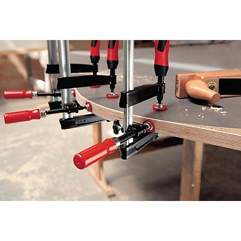 Plusieurs serre-joints maintiennent une pièce de bois courbée en place. Un rabot est à droite.