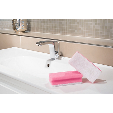Un lavabo blanc avec un robinet chromé. Deux éponges roses sont sur la surface.