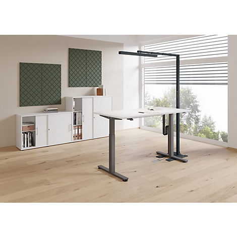 Bureau avec bureau réglable en hauteur, lampe et placards. Parquet clair et panneaux muraux verts.