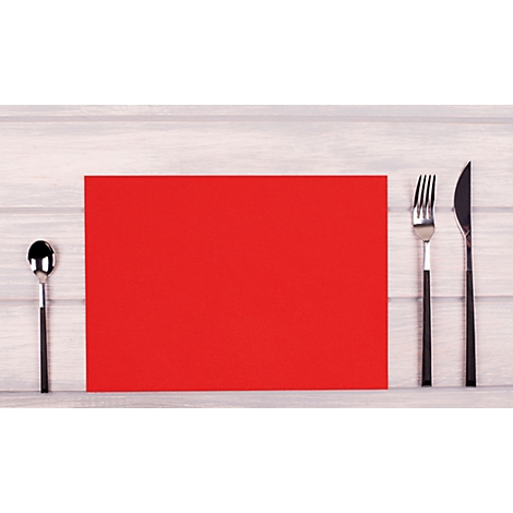Set de table rouge avec des couverts sur fond en bois clair.