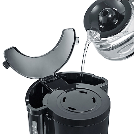Une cafetière noire est remplie d'eau à partir d'une carafe en verre. Le couvercle de la machine est ouvert.