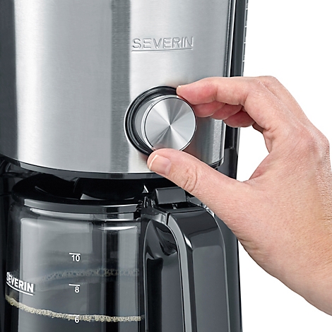 Gros plan sur une cafetière, une main tourne le bouton rotatif argenté à côté d'un récipient en verre avec un indicateur de niveau d'eau.