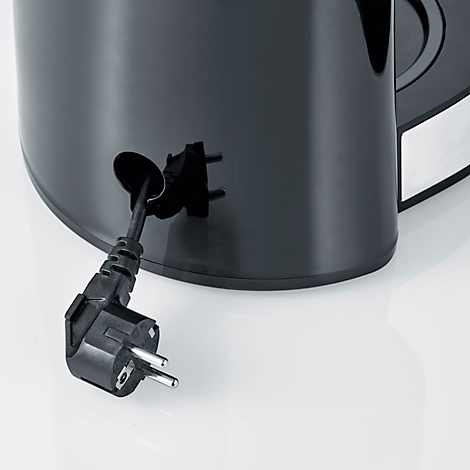 Gros plan : Prise noire dépassant de la cafetière. La prise est passée par un trou. Le fond est gris clair.
