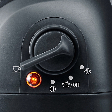 Nahaufnahme: Ein schwarzer Drehknopf einer Kaffeemaschine. Der Knopf steht auf Kaffee-Symbol. Orangefarbenes Licht leuchtet daneben.