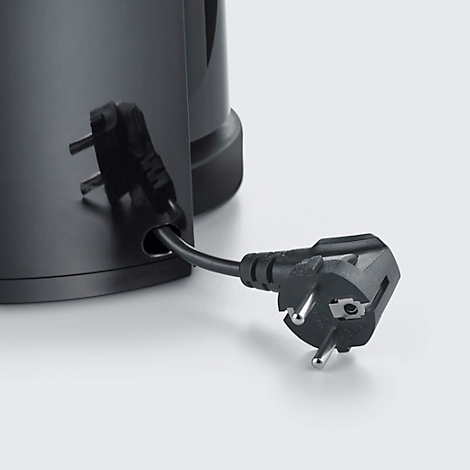 Detailaufnahme: Ein schwarzer Stecker wird in die entsprechende Öffnung eines schwarzen Wasserkochers gesteckt.