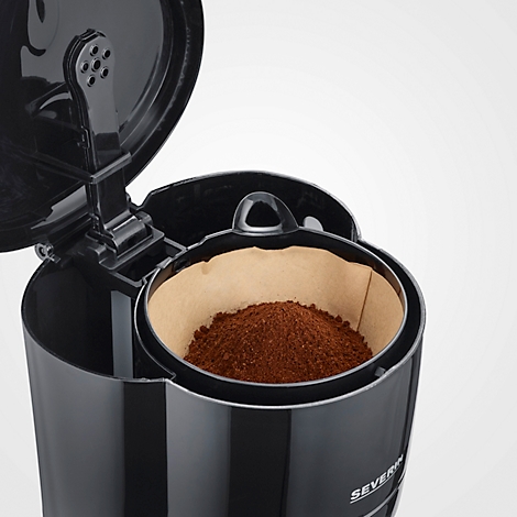 Nahaufnahme einer schwarzen Kaffeemaschine. Im Filter liegt Kaffeepulver. Der Deckel ist halb geöffnet.