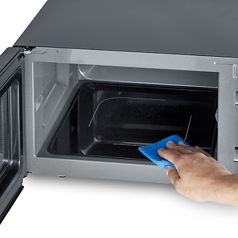 Open microwave being cleaned with a blue cloth. Interior of the microwave is black.