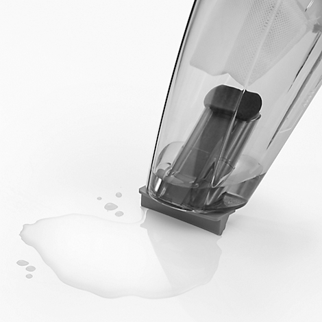 Part of a transparent blender pouring liquid onto a white surface.