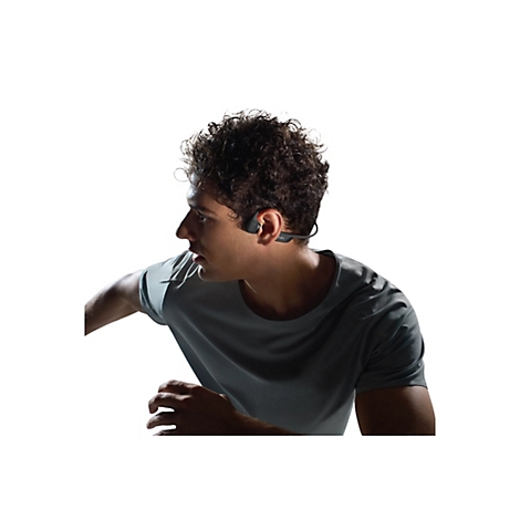 Mann mit lockigem Haar, trägt Sport-Kopfhörer. Er scheint gerade zu rennen, ein graues T-Shirt tragend, vor weissem Hintergrund.